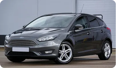 Grauer Ford Focus Kombi, seitliche Frontansicht, parkend vor einer grauen Wand.