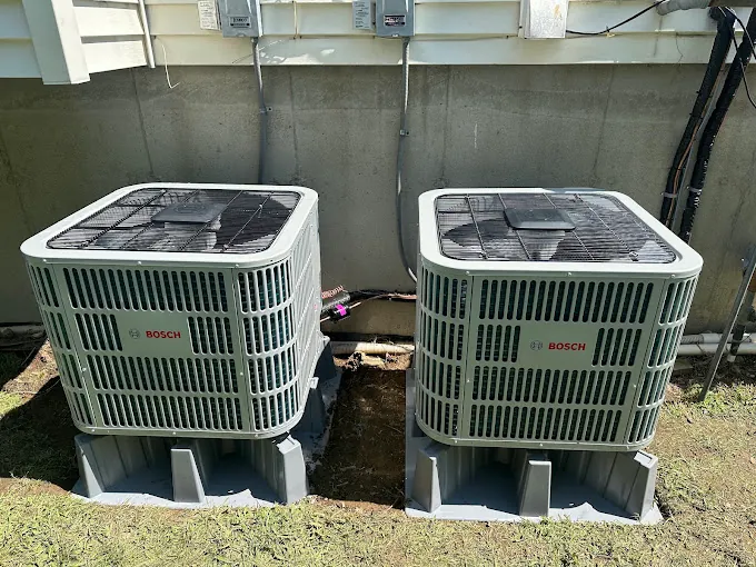 Two Bosch air conditioning units installed side by side on plastic bases outside a building.