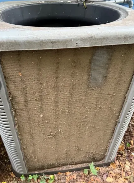 Close-up view of a dirty, clogged air conditioning condenser coil with visible dirt and debris buildup.