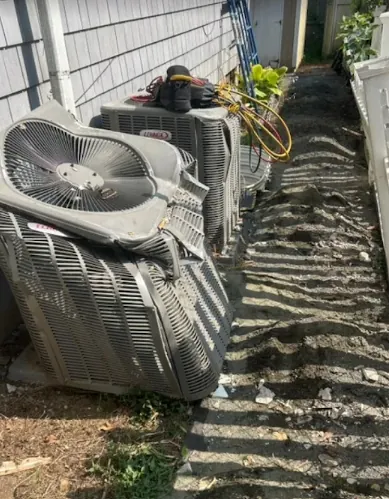 Damaged outdoor air conditioning unit with bent and broken fan blades beside a house.