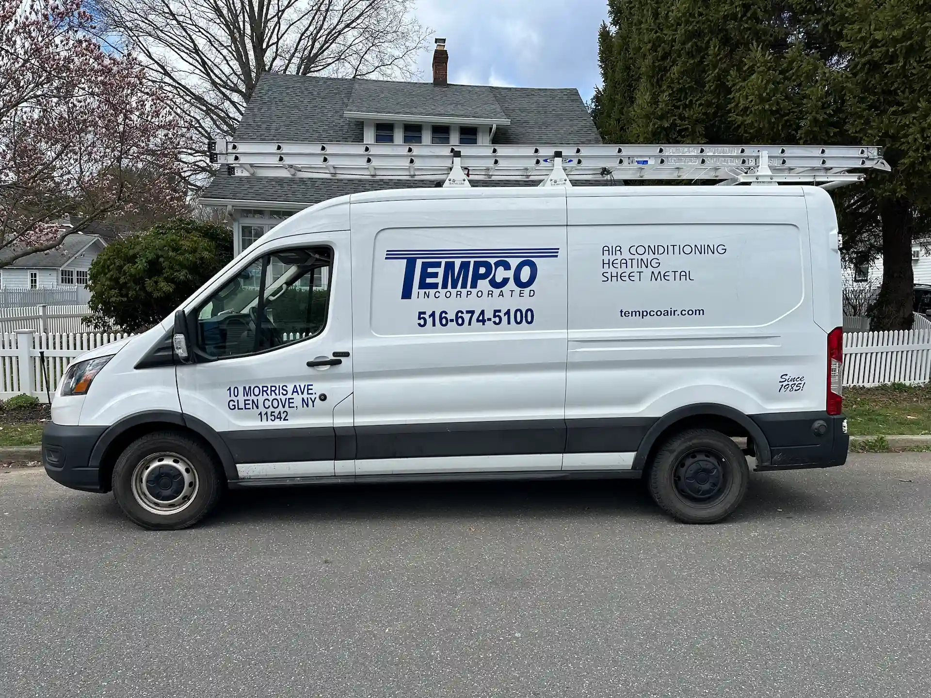 White TEMPCO van with ladders on top parked on a street in front of a house, advertising air conditioning, heating, and sheet metal services.