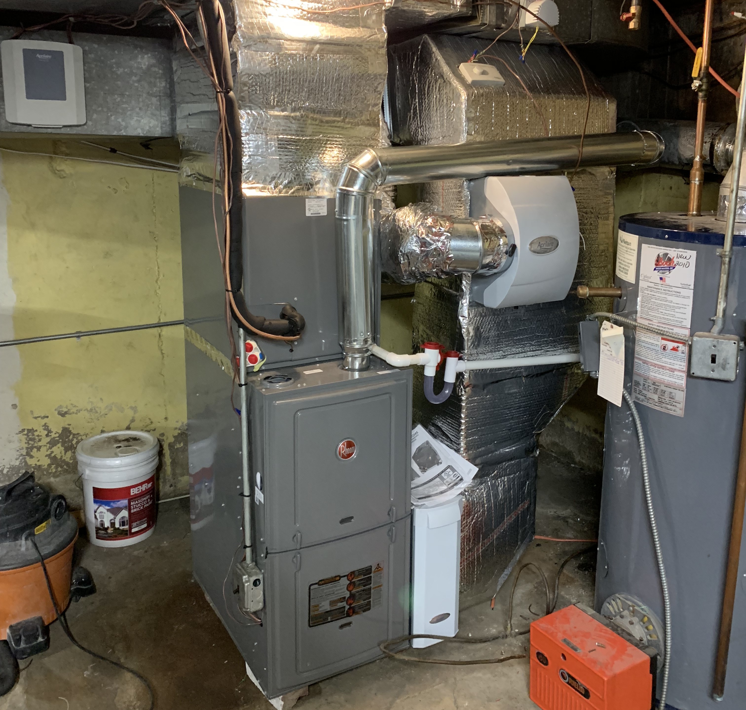 Basement furnace and water heater with insulated ductwork and various tools and equipment around.