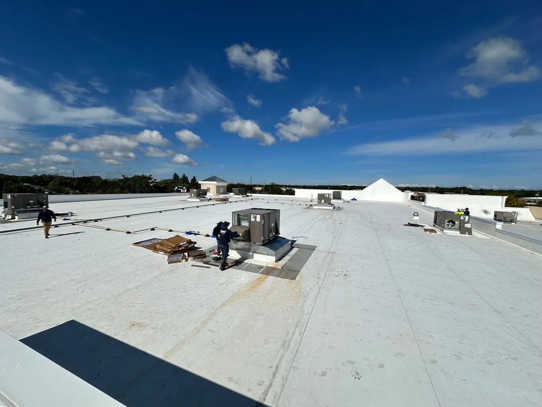 Workers installing HVAC units on a large flat commercial building rooftop under a blue sky with scattered clouds.