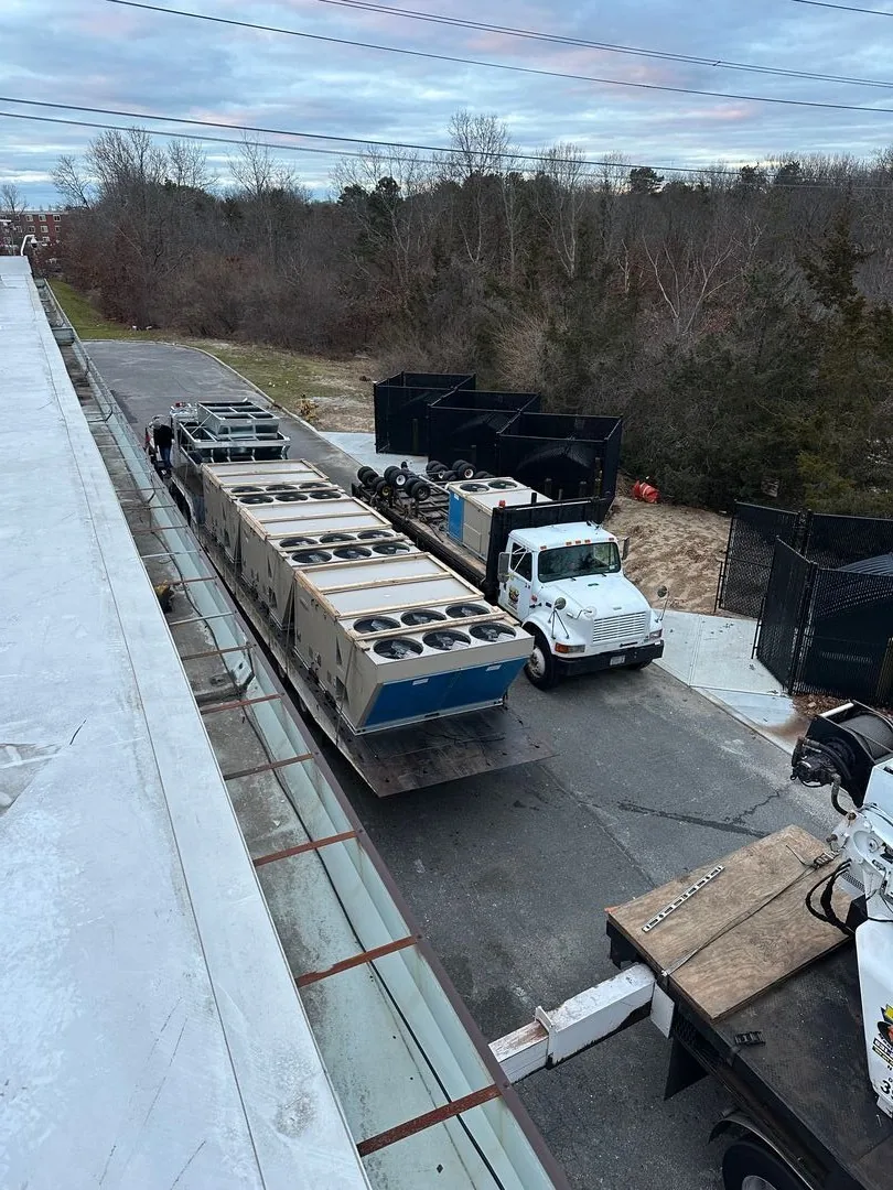 White truck parked on a road next to a building, with large industrial HVAC units loaded on trailers attached to it.