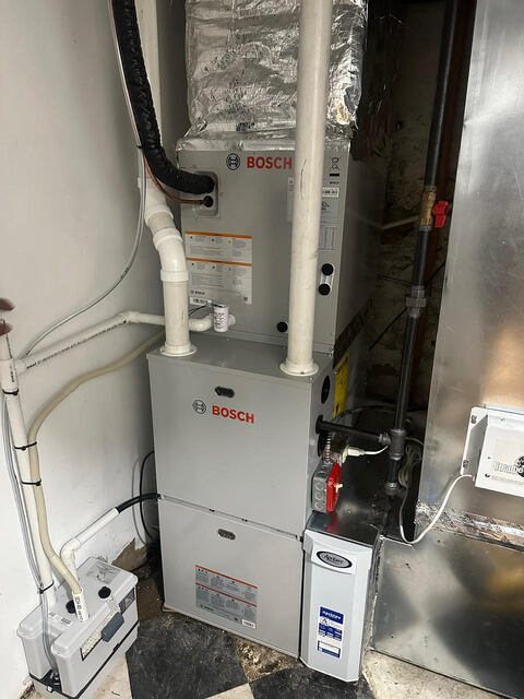 Indoor Bosch heating system unit with attached pipes and ducts in a utility room corner.