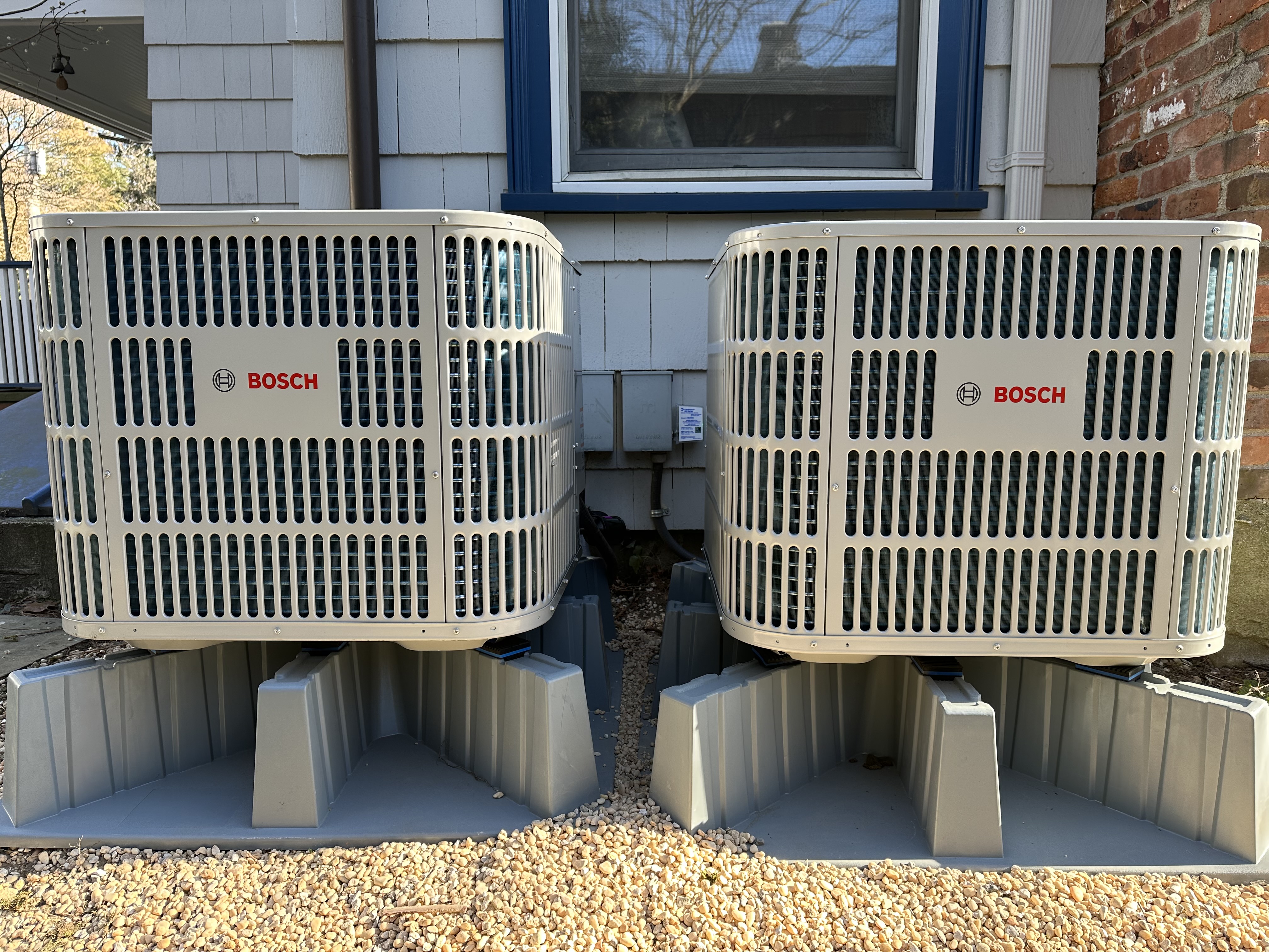 Outdoor Fujitsu Halcyon HFI air conditioning unit mounted on a gravel bed in front of a beige house wall.