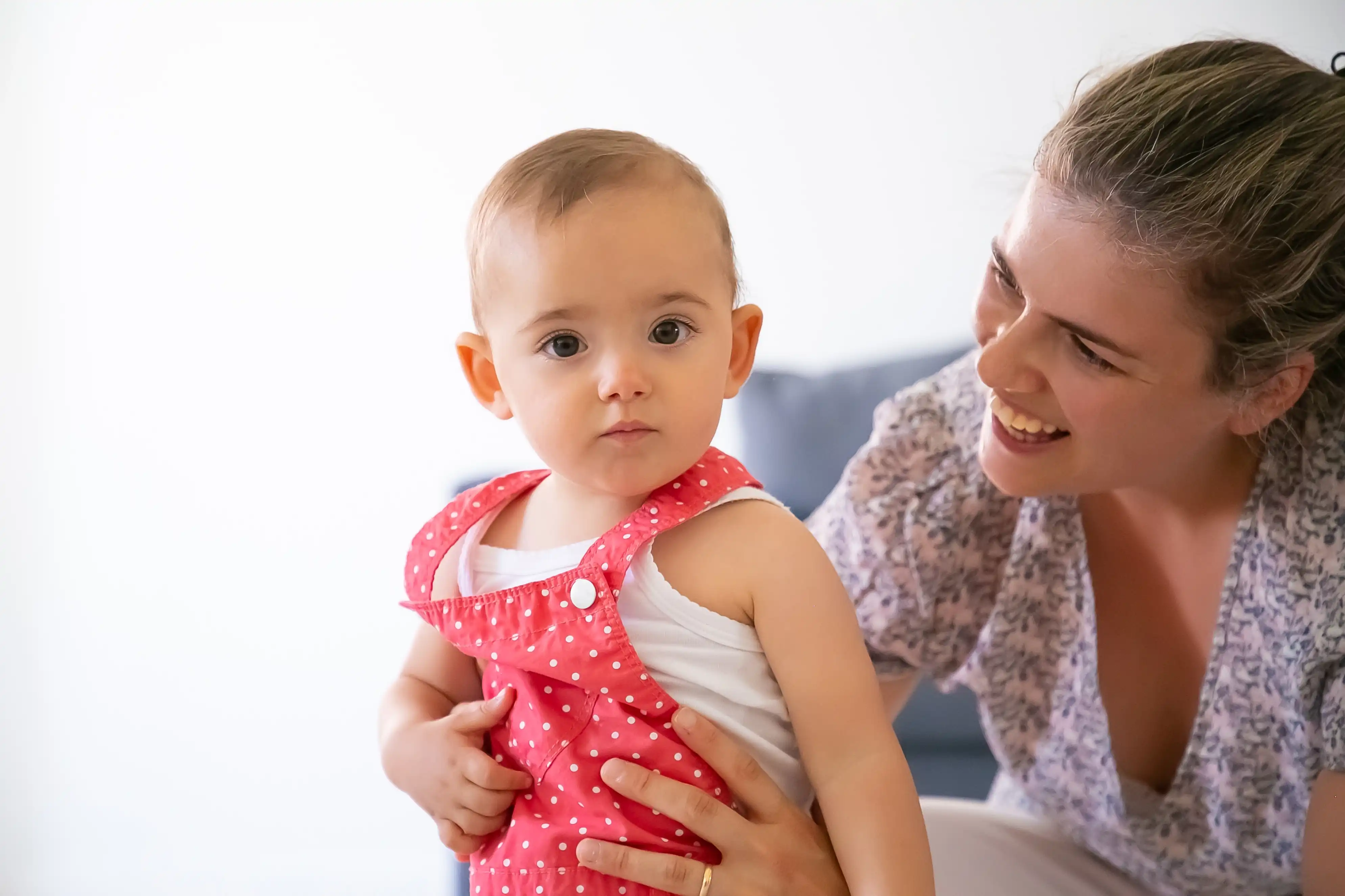 happy-mother-holding-baby-girl-smiling-looking-her-serious-adorable-toddler-red-dungarees-shorts-pretty-mom-talking-with-kid-family-time-motherhood-concept