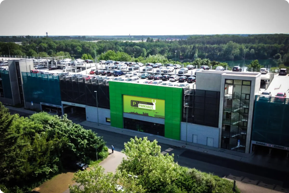 Mehrstöckiges Parkhaus mit grüner Fassade, voller geparkter Autos und umgeben von Bäumen.