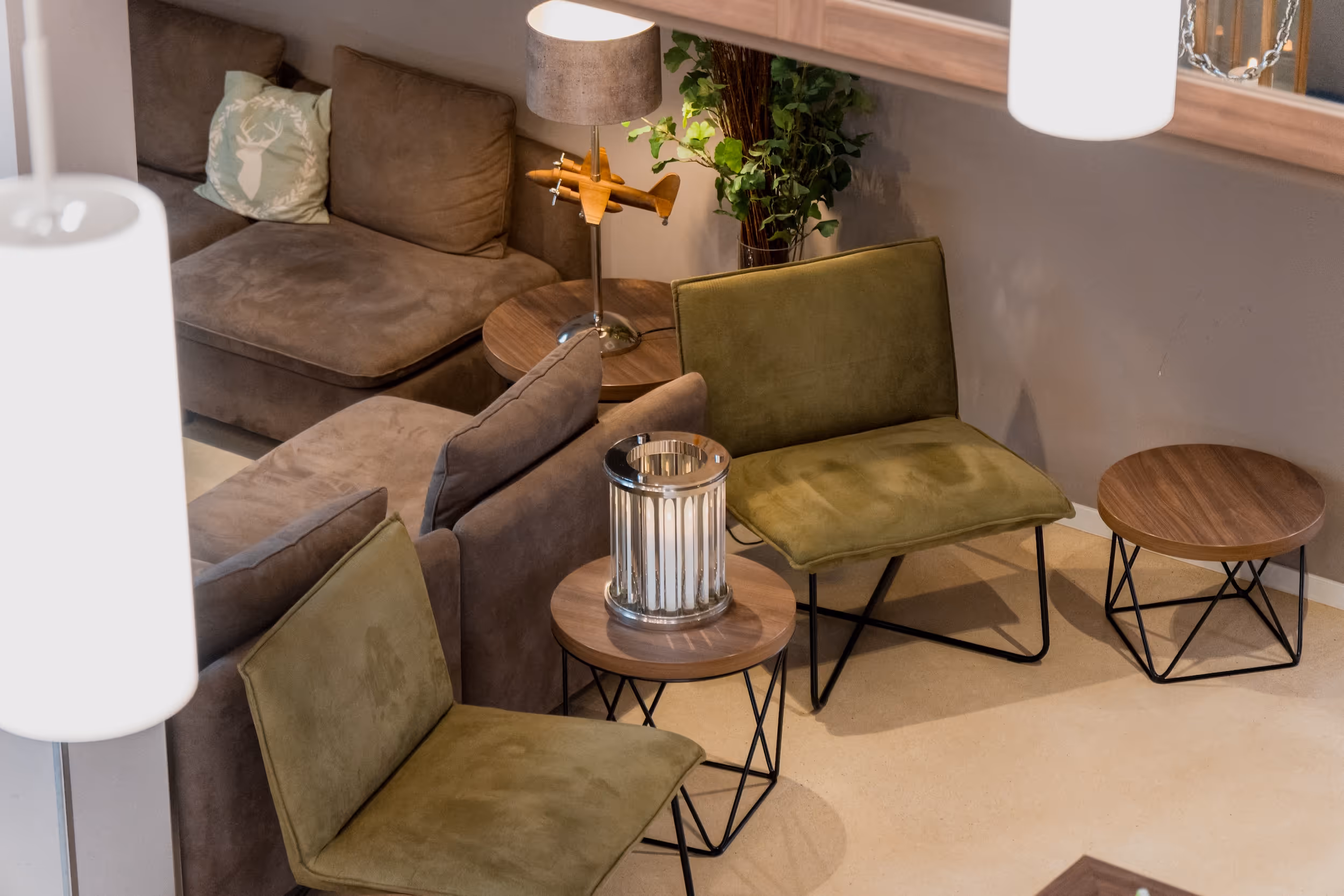 Gemütlicher Sitzbereich mit grünen Sesseln, braunem Sofa, Holz-Beistelltischen und moderner Dekoration.