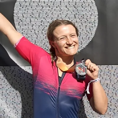 Smiling woman in a pink and blue sports outfit holding a medal and raising one arm in celebration.