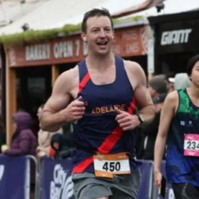Male runner wearing a navy and orange sleeveless top with race number 450, participating in an outdoor race event.