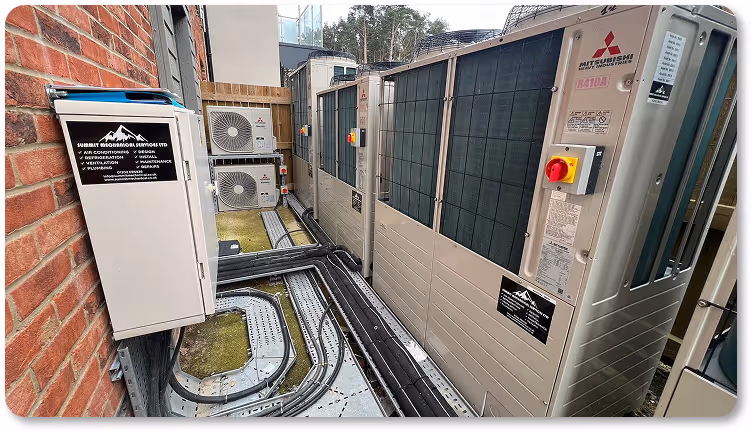 Outdoor mechanical service area with Mitsubishi HVAC units and electrical control panels mounted on a brick wall by Summit Mechanical Services Ltd.
