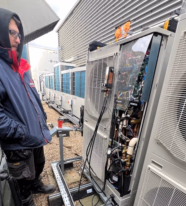 Summit Mechanical Technician in a dark jacket and glasses inspecting the open panel of a large outdoor HVAC unit on a gravel rooftop.