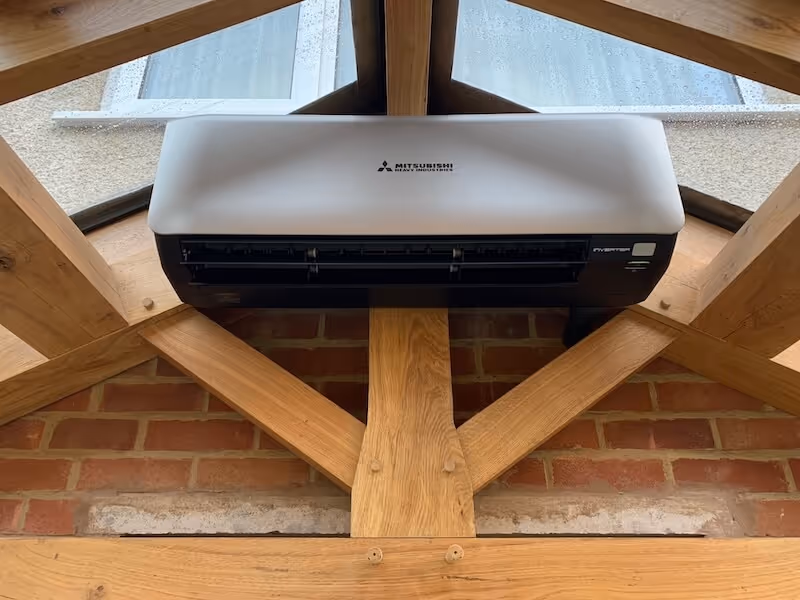 Mitsubishi Heavy Industries air conditioning unit mounted on wooden beams under a glass roof with a brick wall background.
