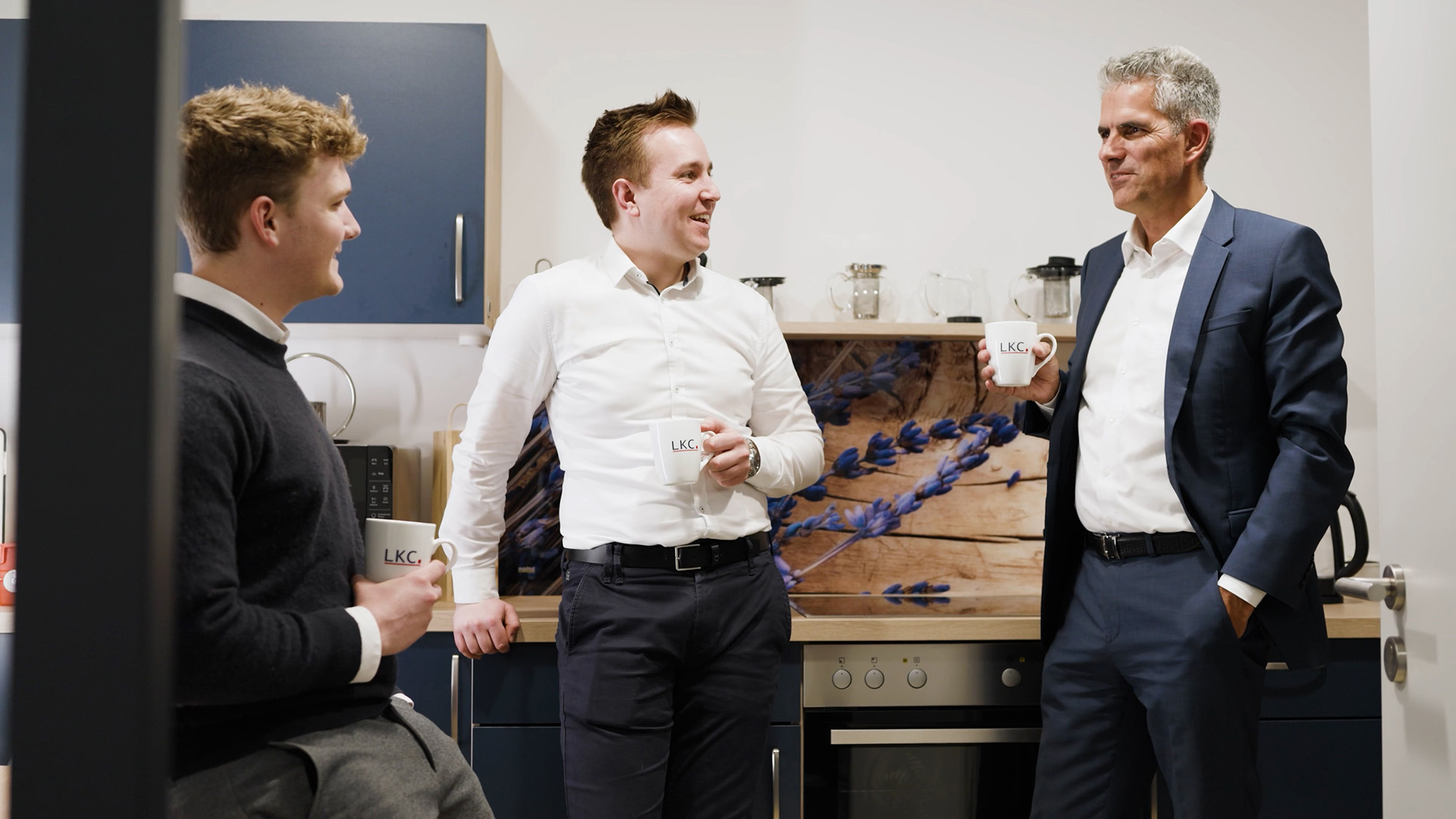 Drei Männer im Business-Outfit stehen draußen und unterhalten sich.