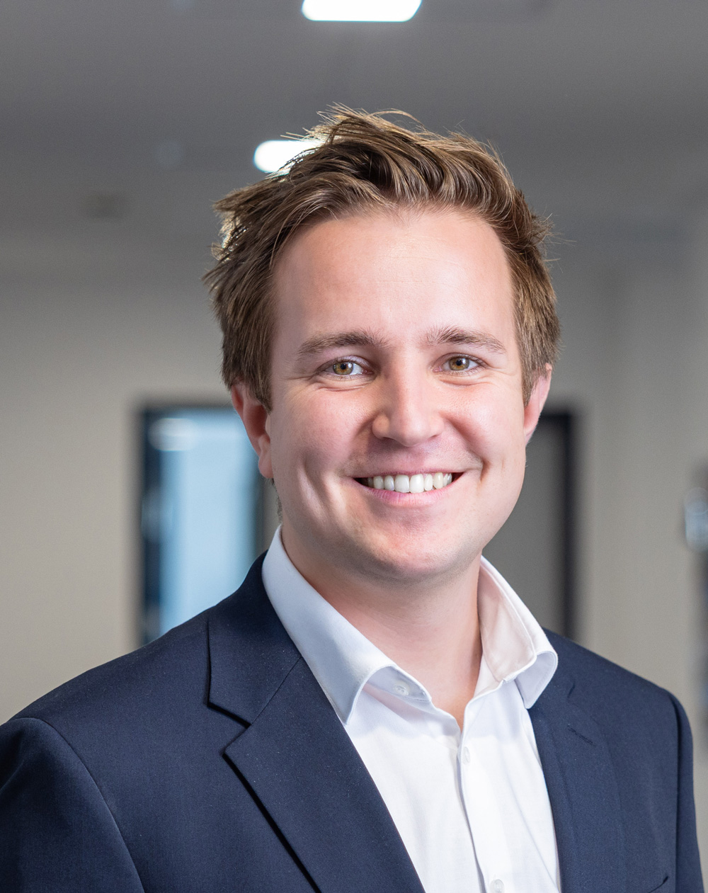 Mann im Anzug mit hellem Hemd lächelt in die Kamera.