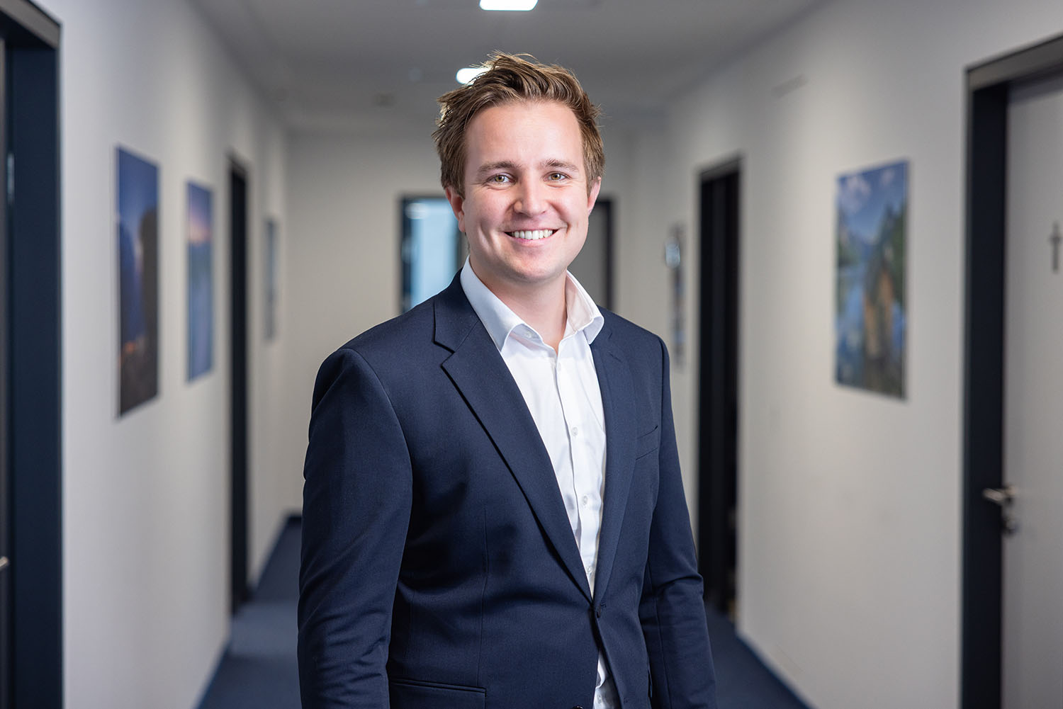 Mann im Business-Outfit steht im Flur und lächelt.