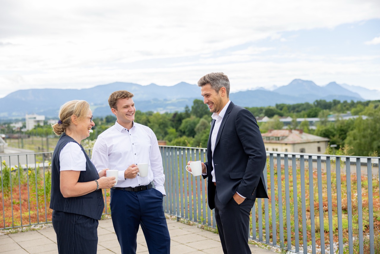 Drei Personen im Anzug im Gespräch auf einer Dachterrasse.