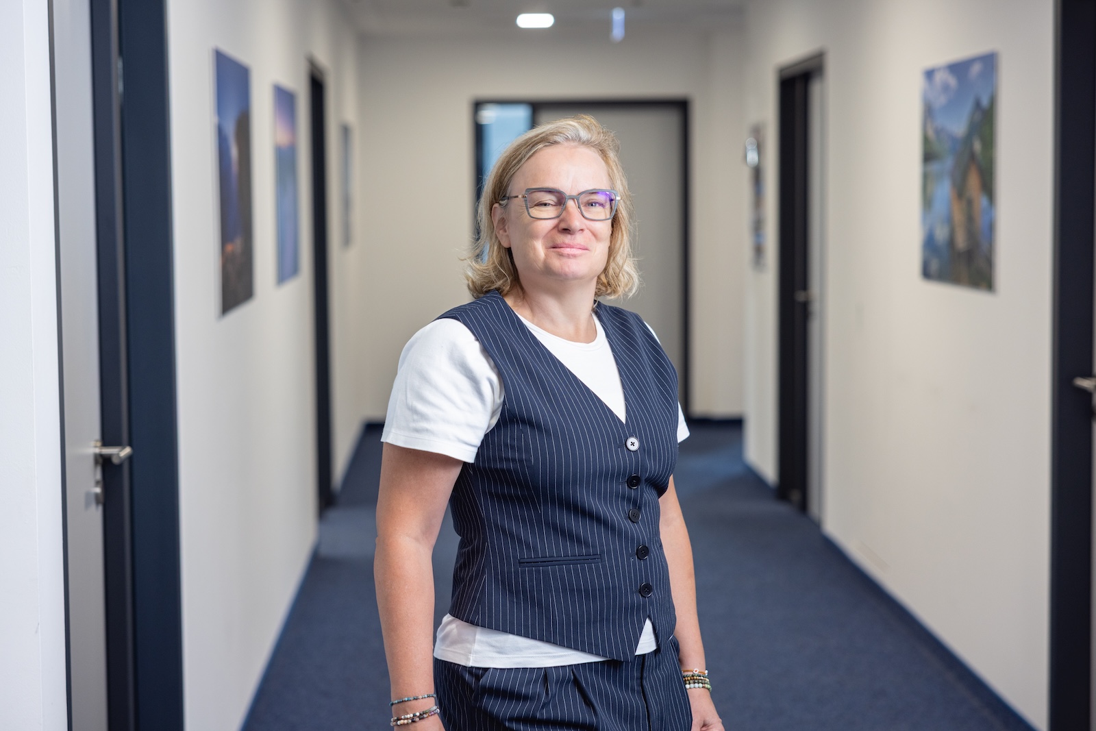 Frau steht in einem Flur, lächelt in die Kamera.