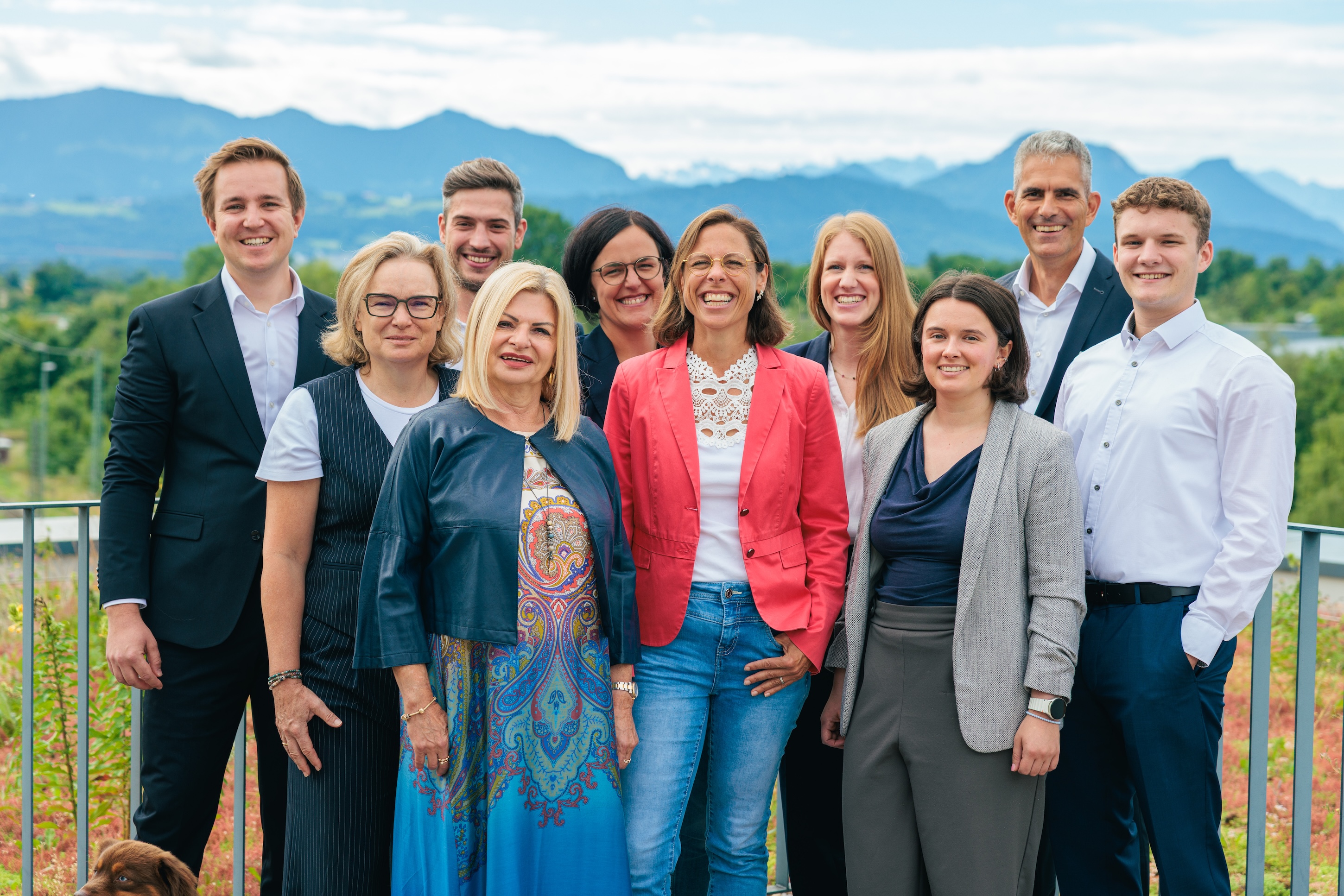 Gruppenfoto von acht Personen draußen vor Landschaftskulisse, alle lächeln in die Kamera.