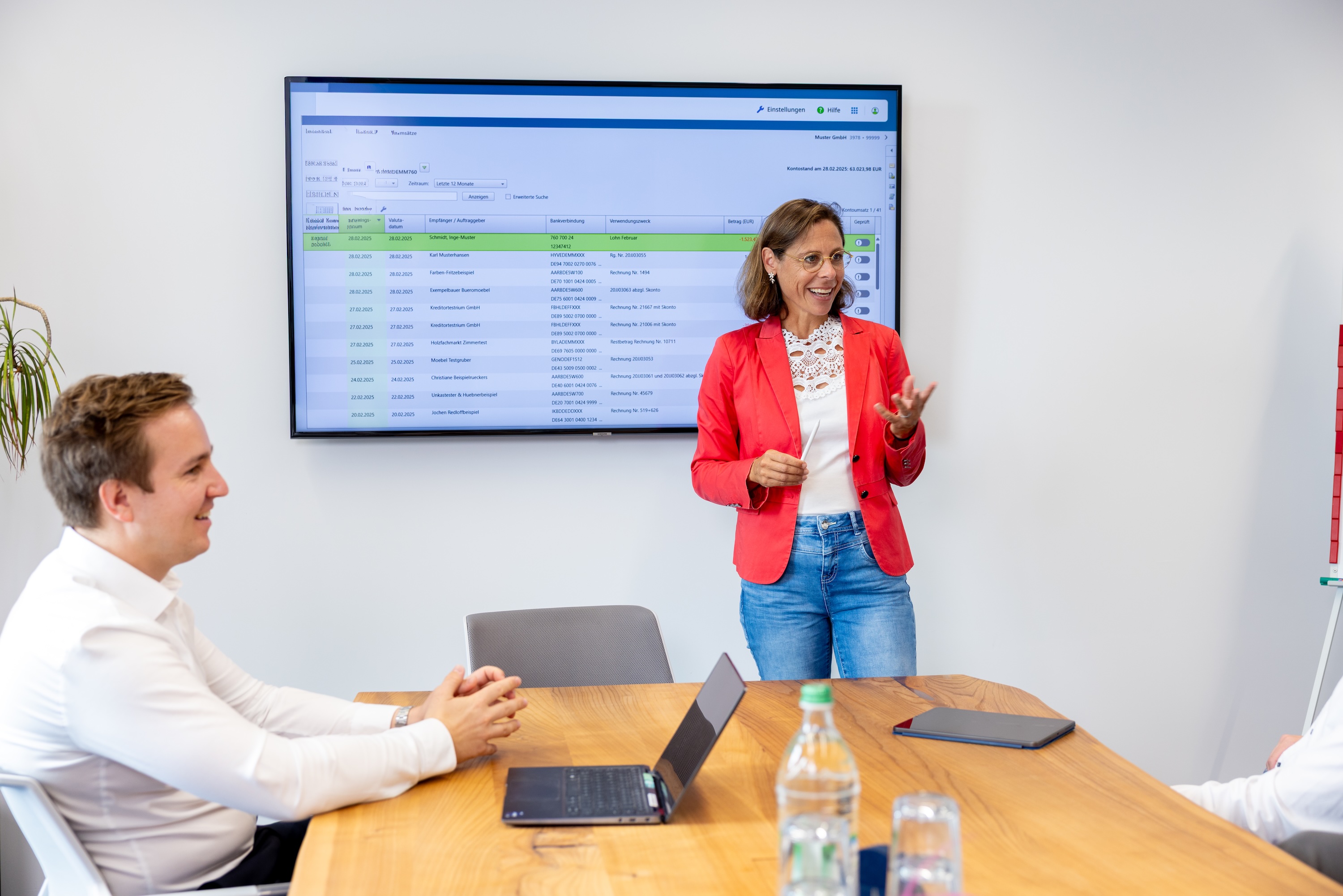 Frau steht vor einem Bildschirm und präsentiert einer Gruppe etwas.