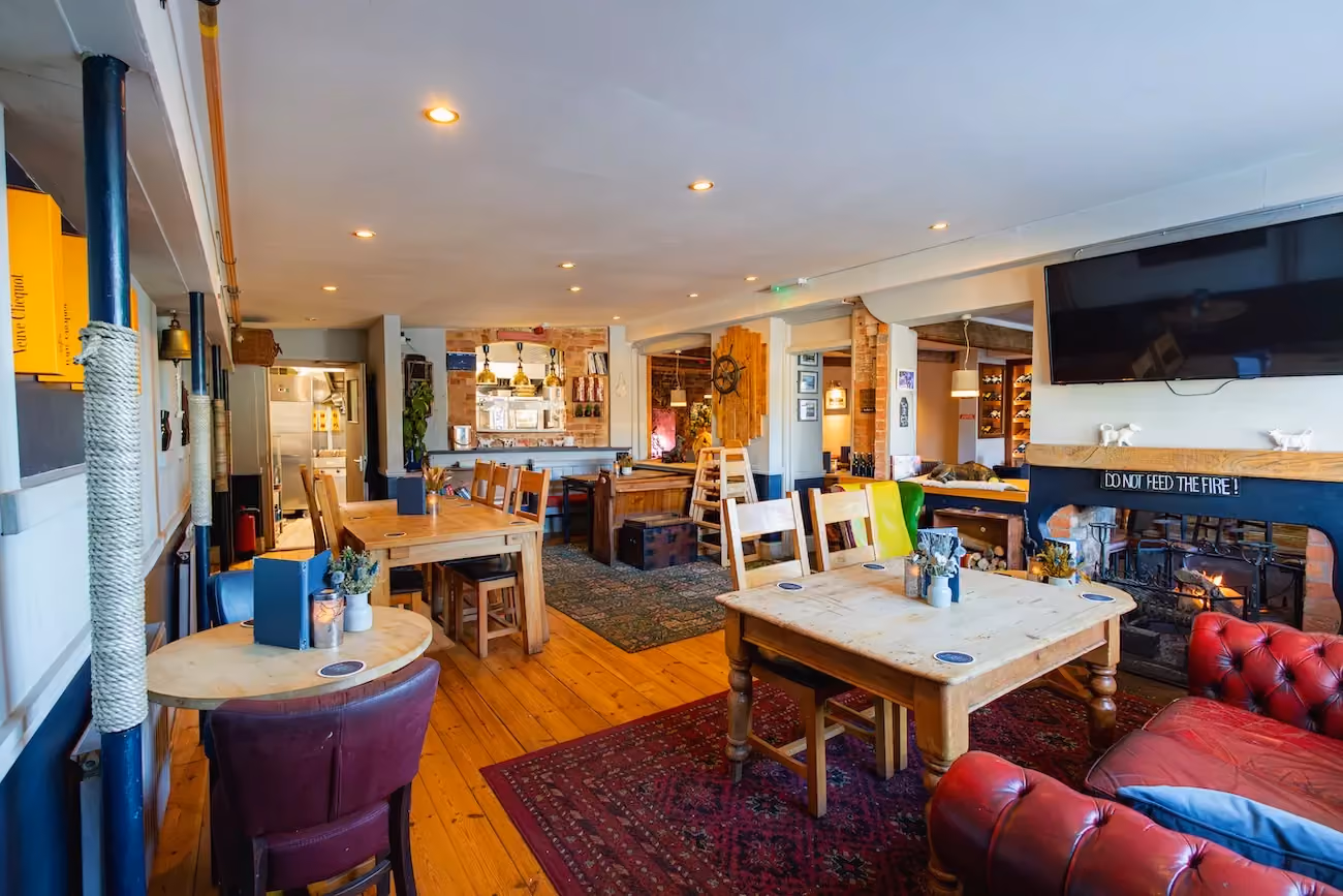 Cosy pub interior at The Bridge Inn & Ferry with wooden dining tables, a lit open fireplace and leather sofas