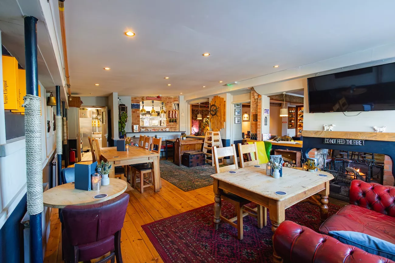 Cosy pub interior at The Bridge Inn & Ferry with wooden dining tables, a lit open fireplace and leather sofas
