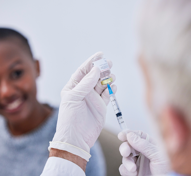 Healthcare worker prepares a vaccine syringe while a patient smiles nearby as part of a community vaccination campaign.