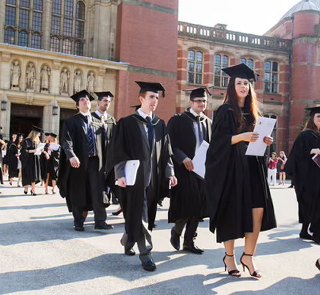 Students in graduation gowns walking across the University of Birmingham campus during a commencement ceremony.