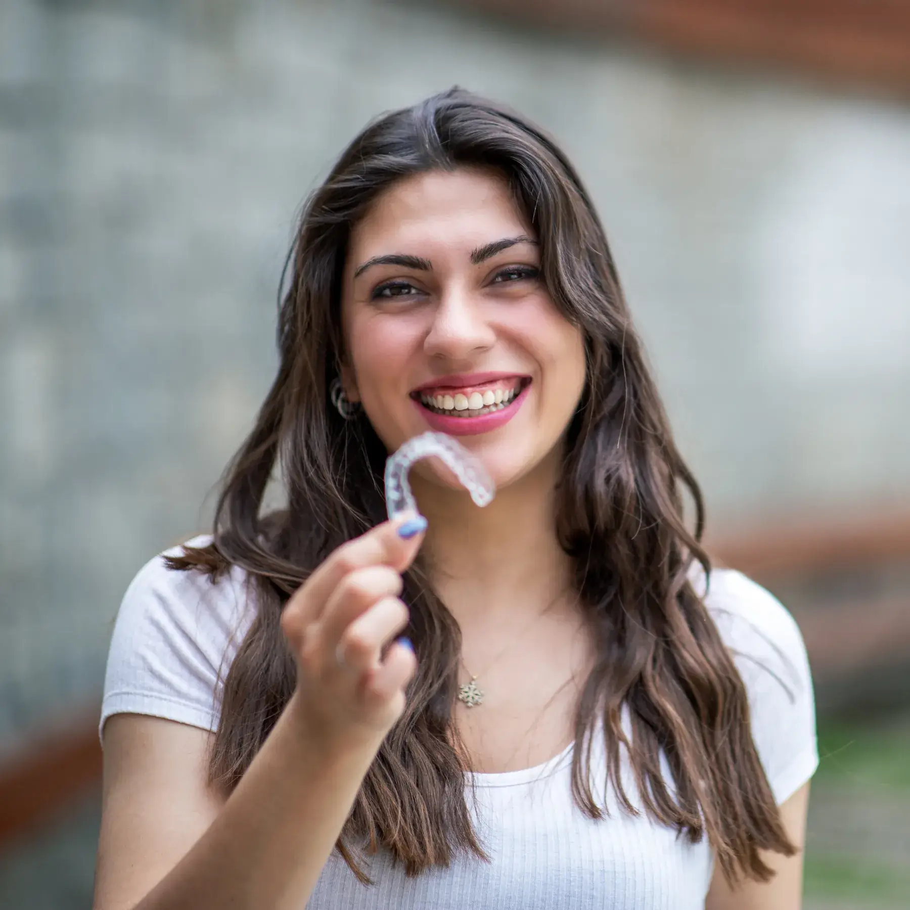 Woman smiling and holding a clear dental aligner in her hand.