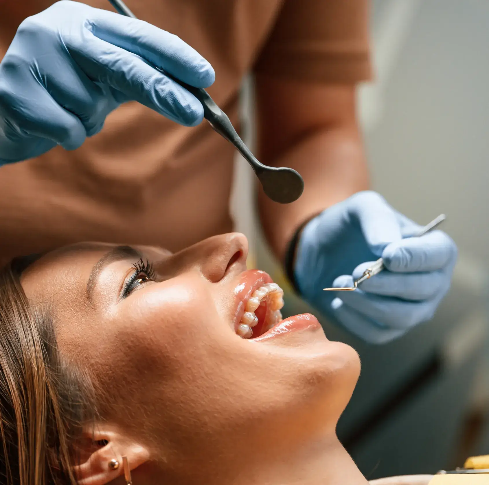 A dentist examines a smiling patient's teeth with dental tools in a clinic.