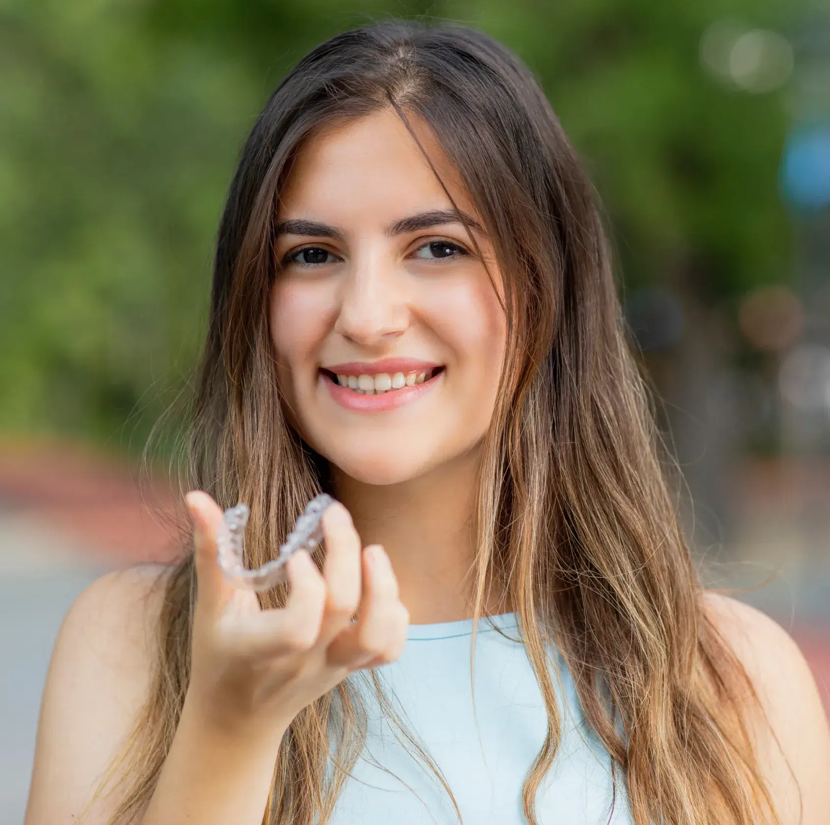 A woman smiling and holding a dental aligner in her hand.