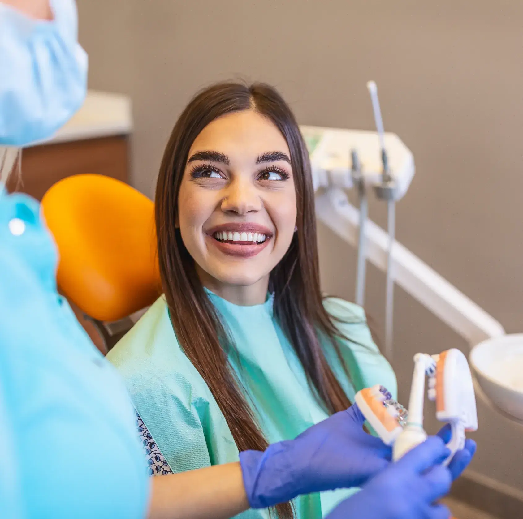 A woman sits in a dental chair, smiling while a dentist holds a dental model.
