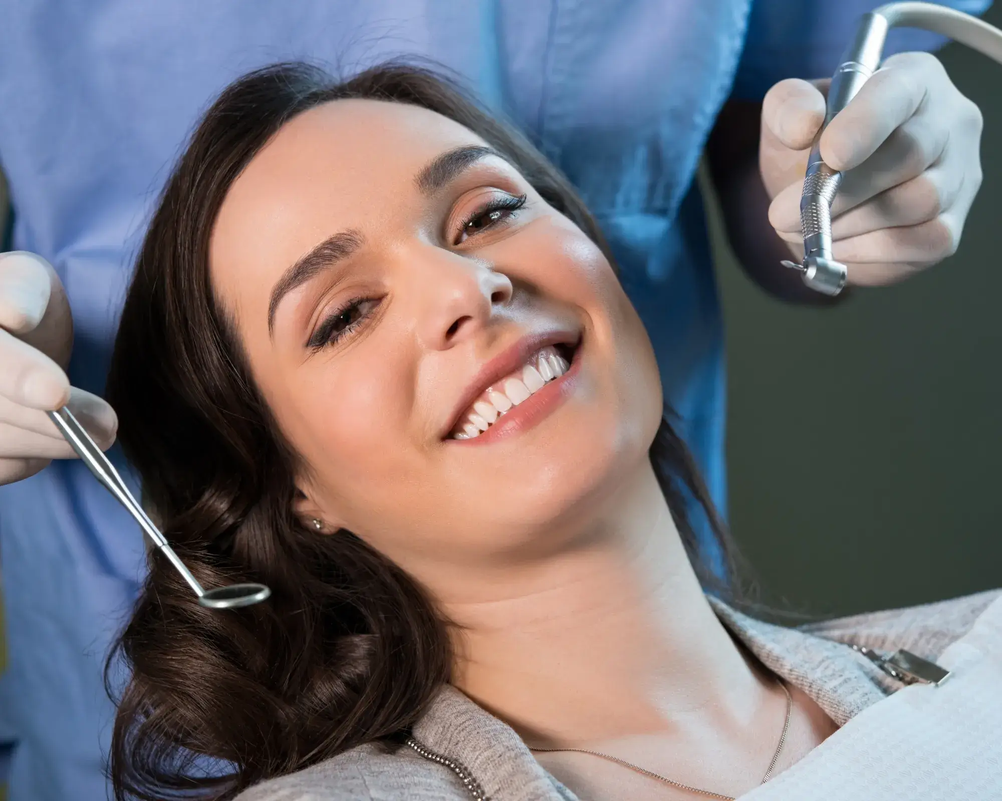 A woman smiles in a dental chair while a dentist holds tools nearby.