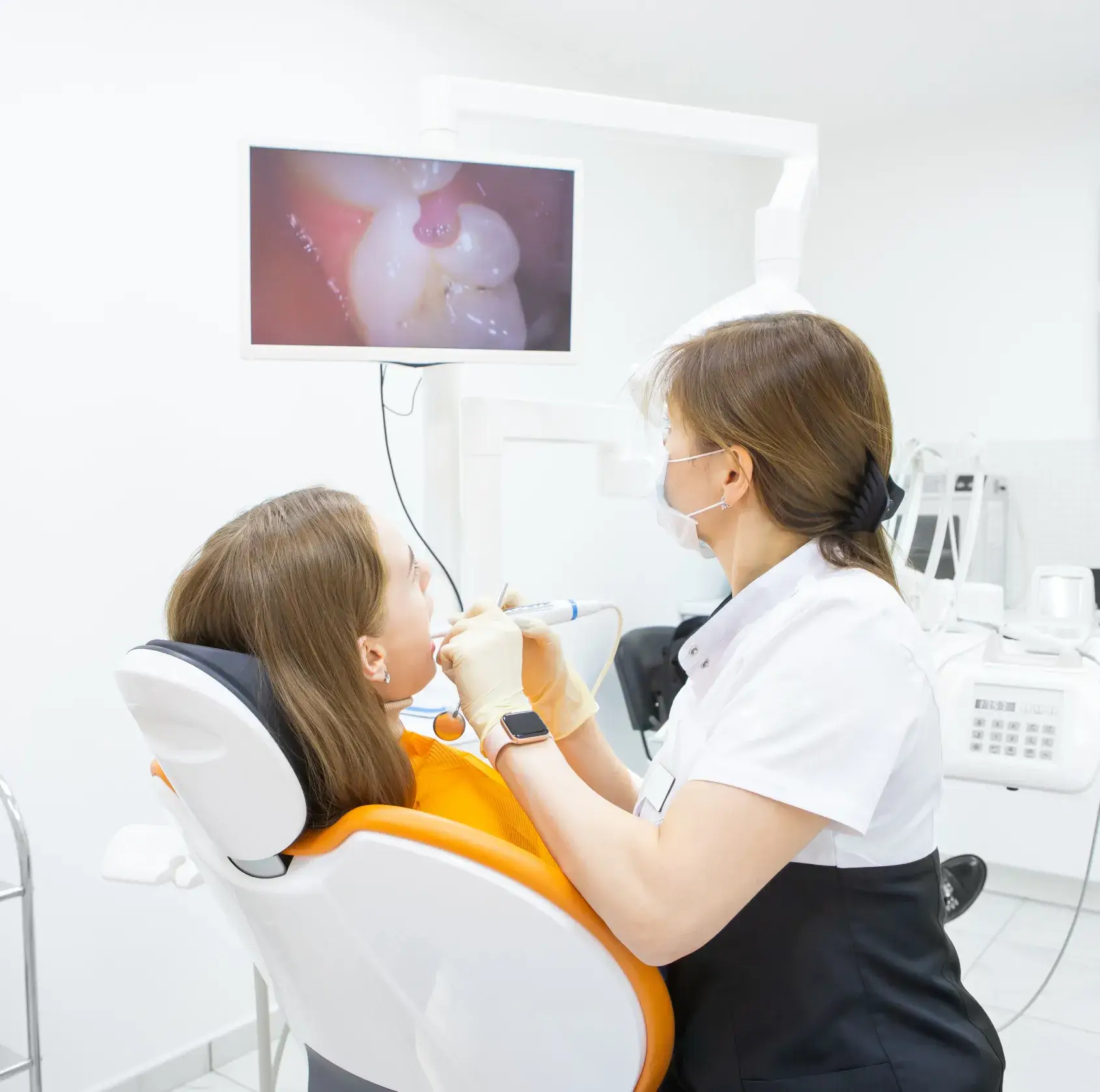 A dentist examines a patient's teeth on a monitor during a dental appointment.