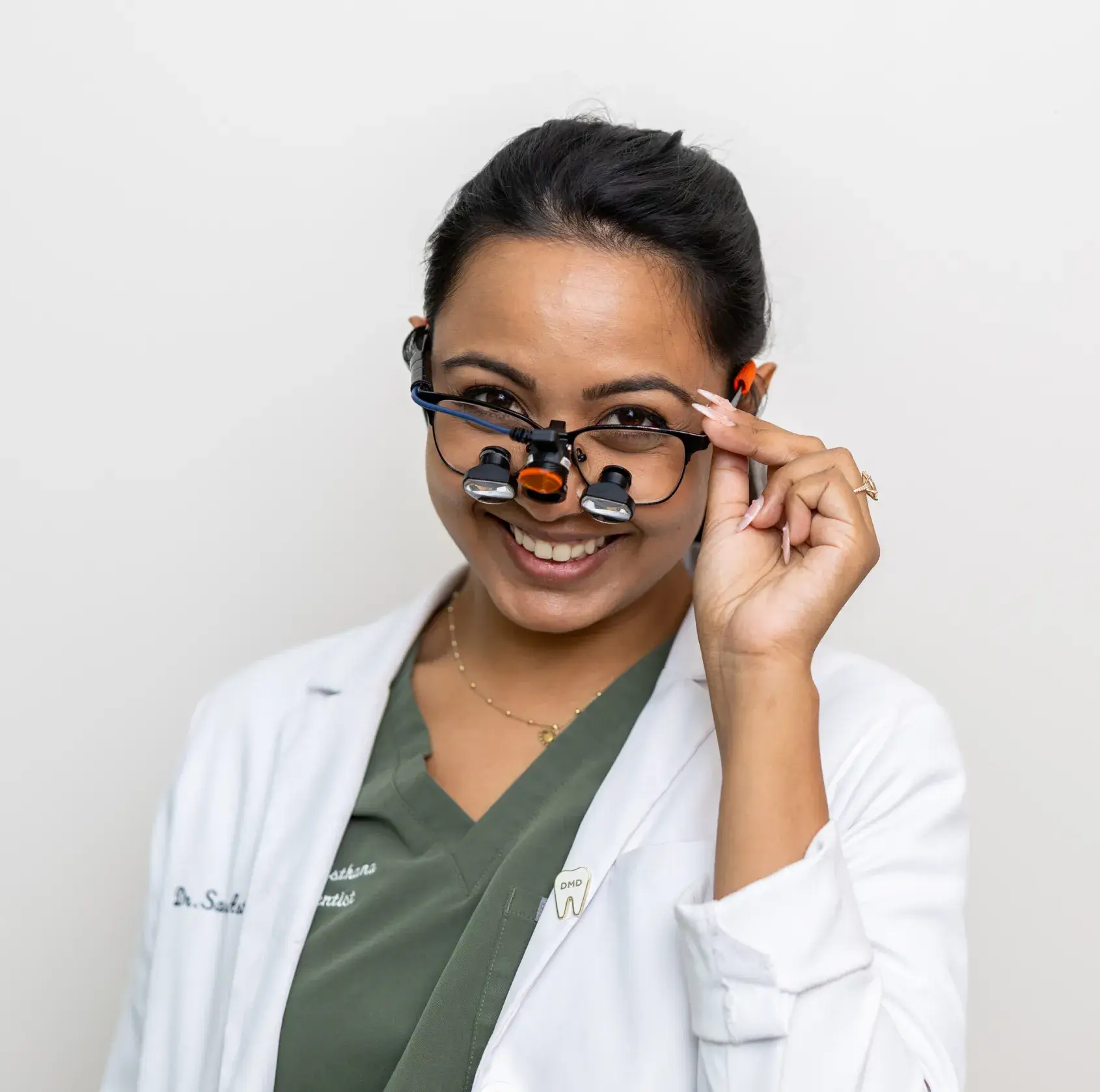 Smiling female dentist wearing magnifying glasses and a white coat.