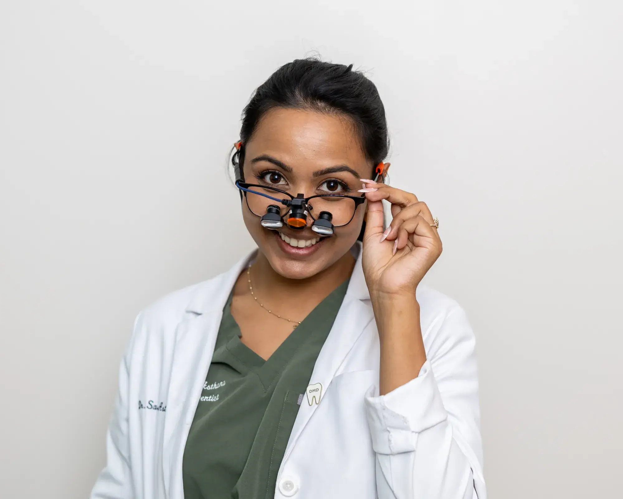 Smiling female dentist wearing a white coat and dental loupes on glasses.