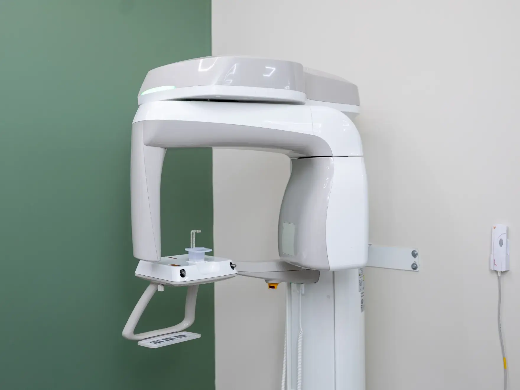 Dental panoramic X-ray machine mounted on a wall with green and white background.