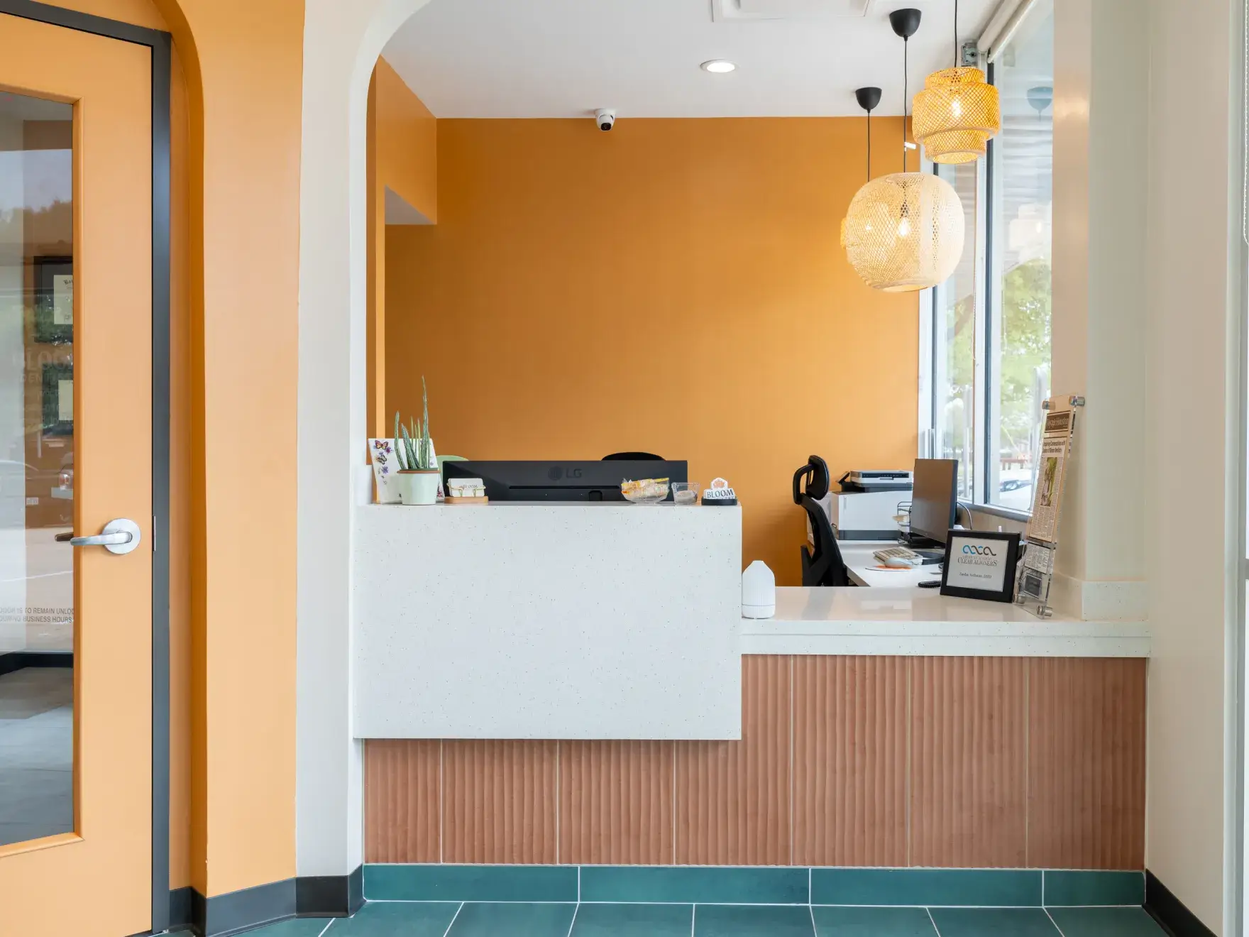 Reception desk area with modern decor, orange walls, green floor tiles, and hanging woven light fixtures.