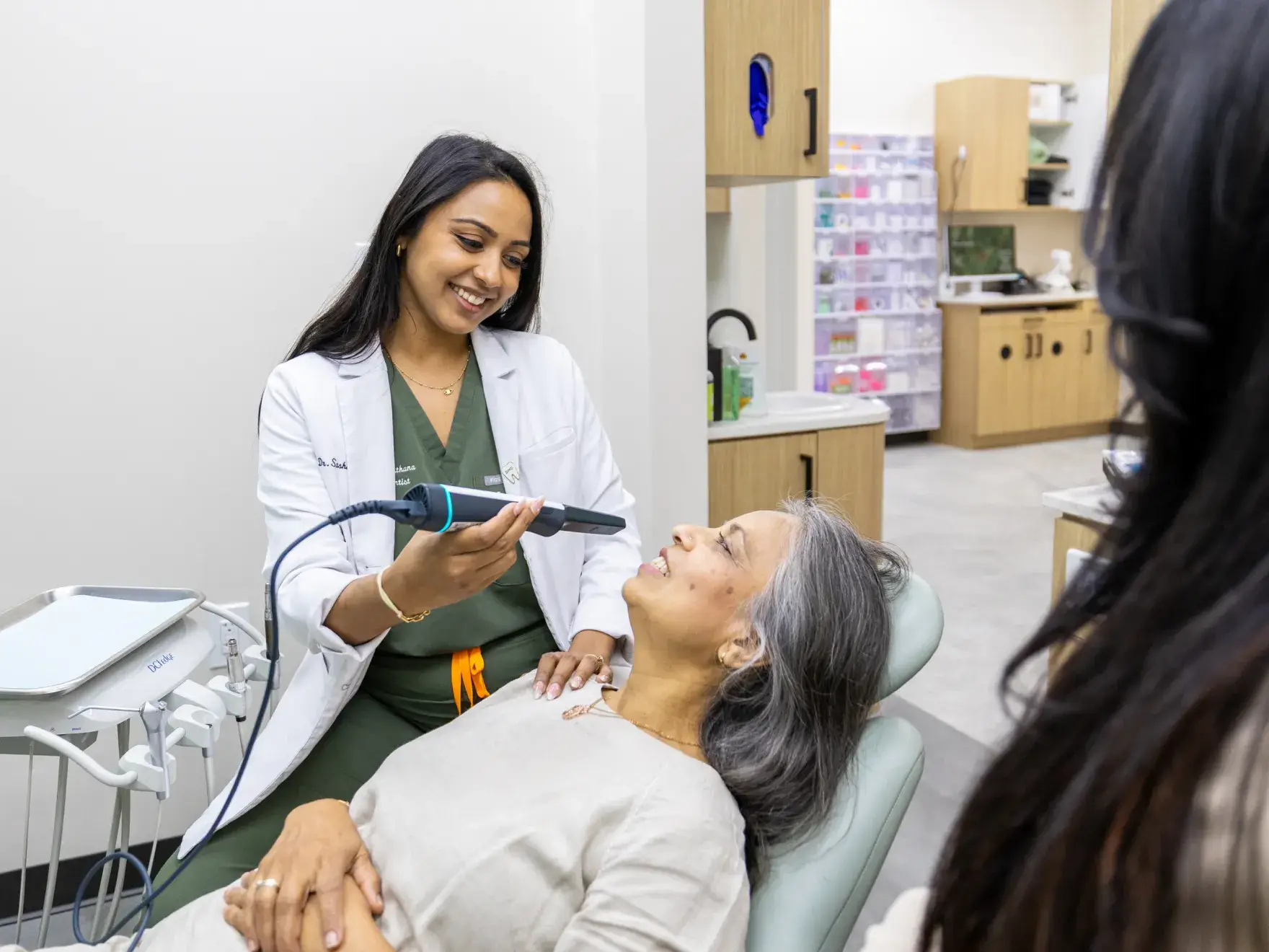 Dentist smiling and holding a dental scanner near a relaxed patient reclining in a dental chair.