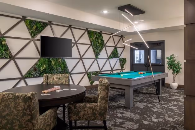 Interior amenity room at Risor Apple Valley featuring a pool table, card table, geometric living wall with embedded greenery, and pendant lighting designed by Kaas Wilson Architects for active 55+ senior living.