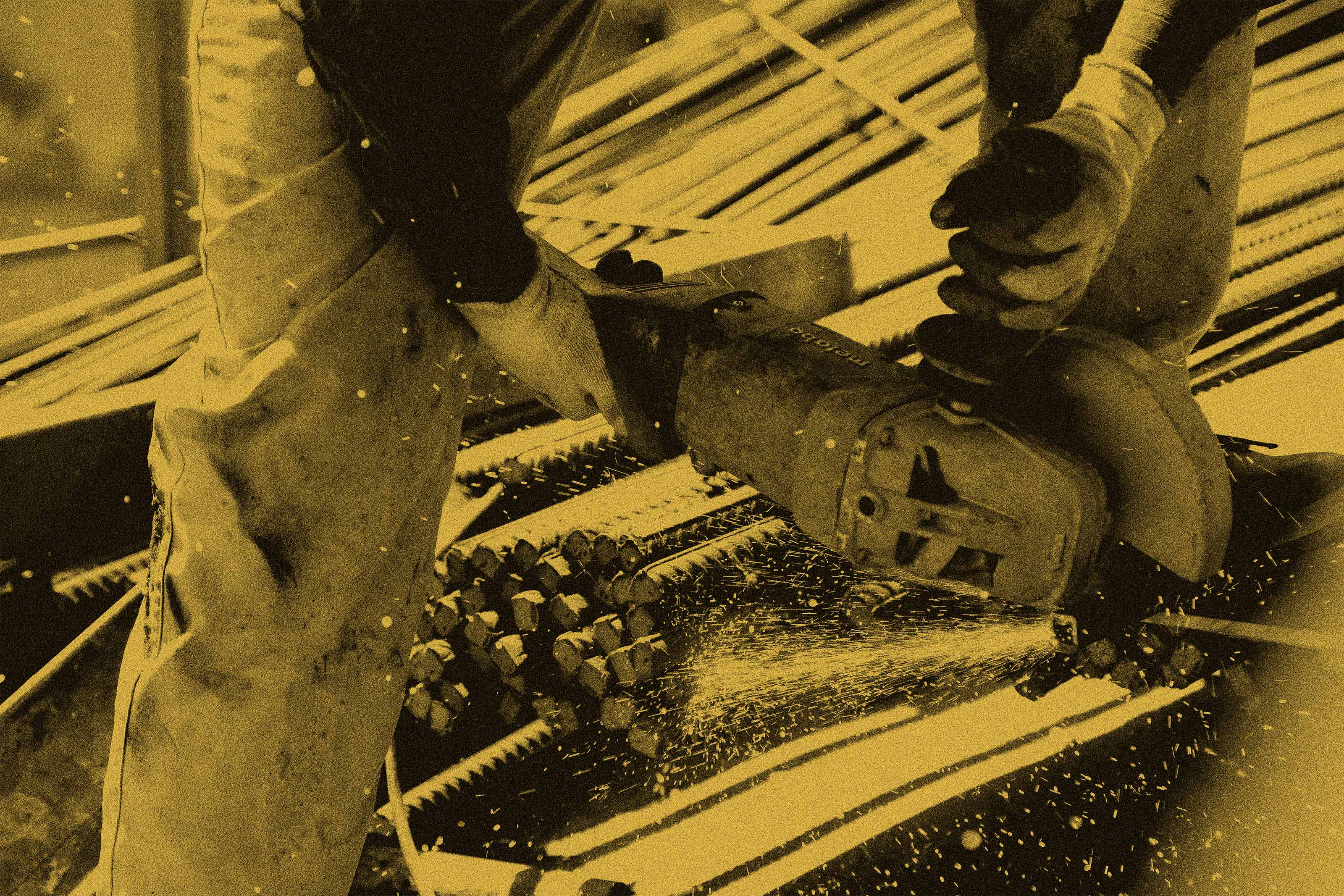 Worker using an electric angle grinder to cut metal rods, with sparks flying in a construction setting.