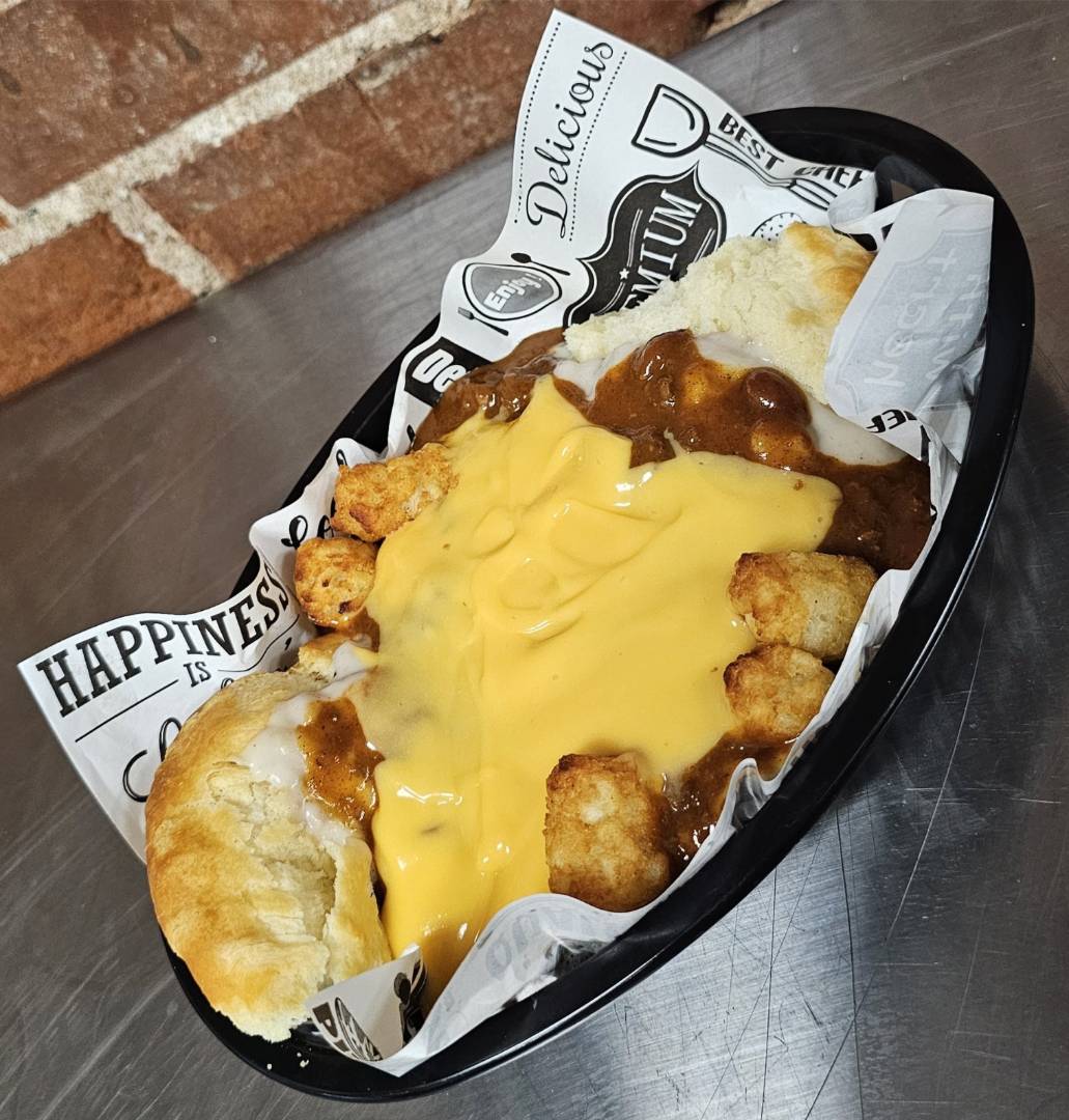 A black bowl filled with crispy tater tots, smothered in melted cheese and savory gravy.