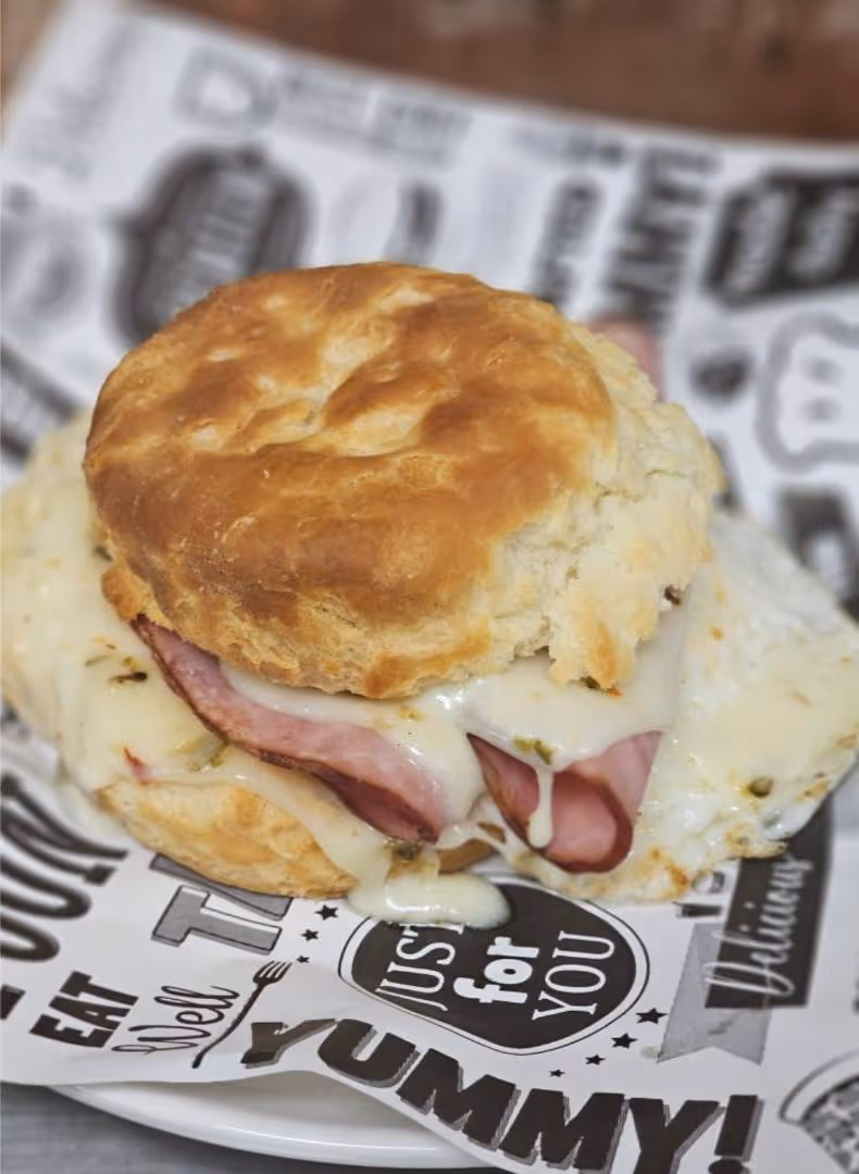 A freshly baked biscuit sandwich with melted cheese and ham, placed on patterned paper.