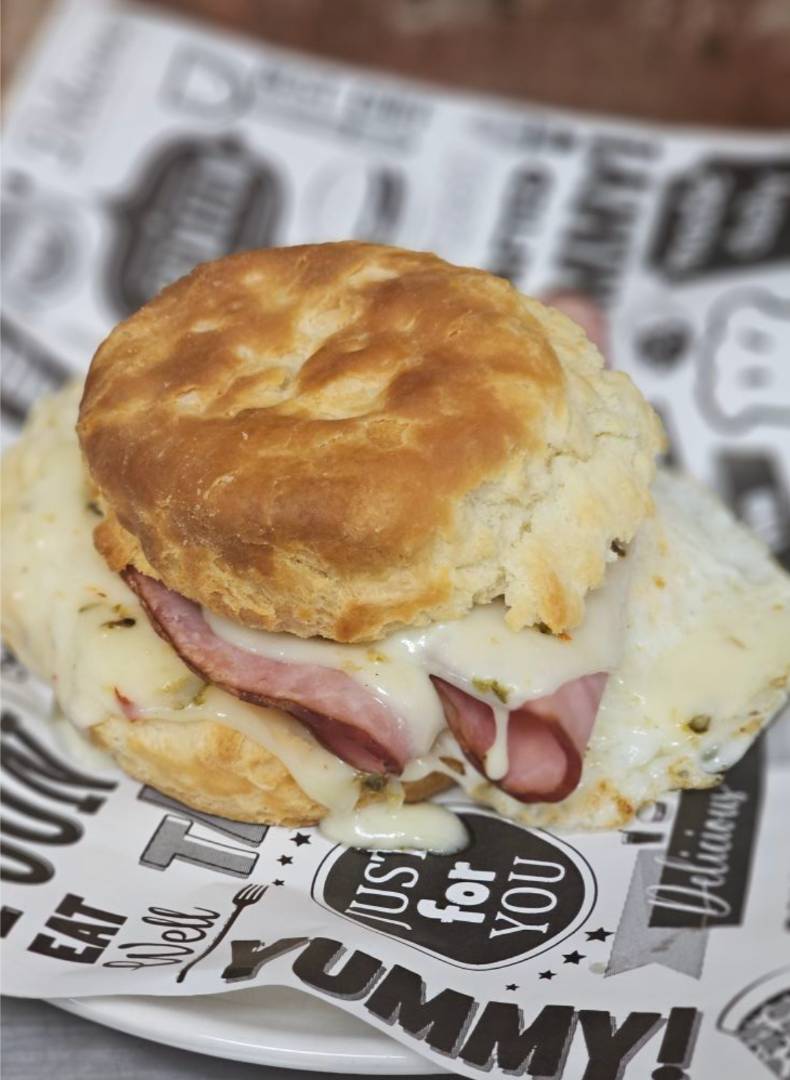 A freshly baked biscuit sandwich with melted cheese and ham, placed on patterned paper.