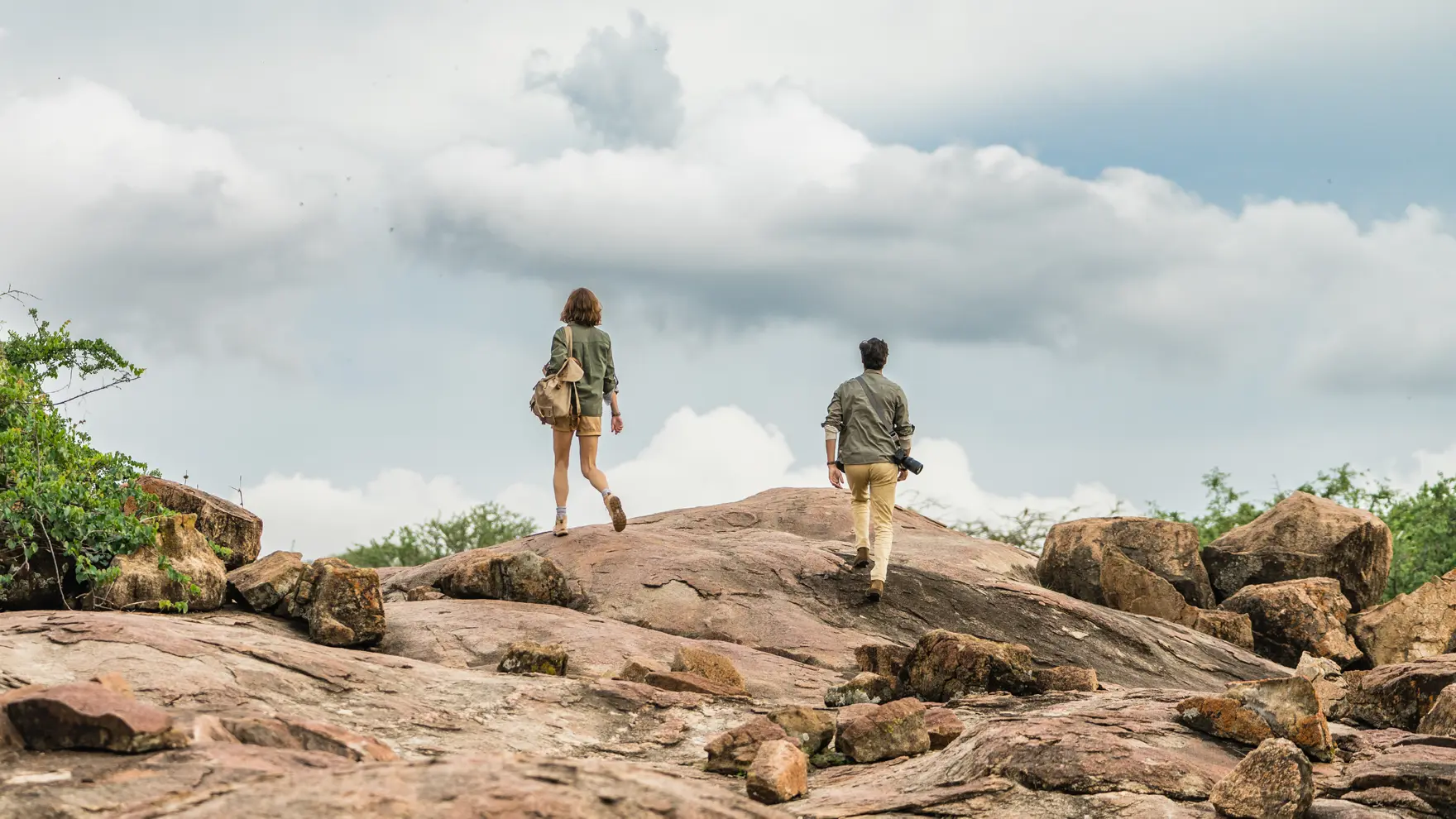 Two travelers walking across a rocky outcrop under a cloudy sky during a guided wilderness exploration.