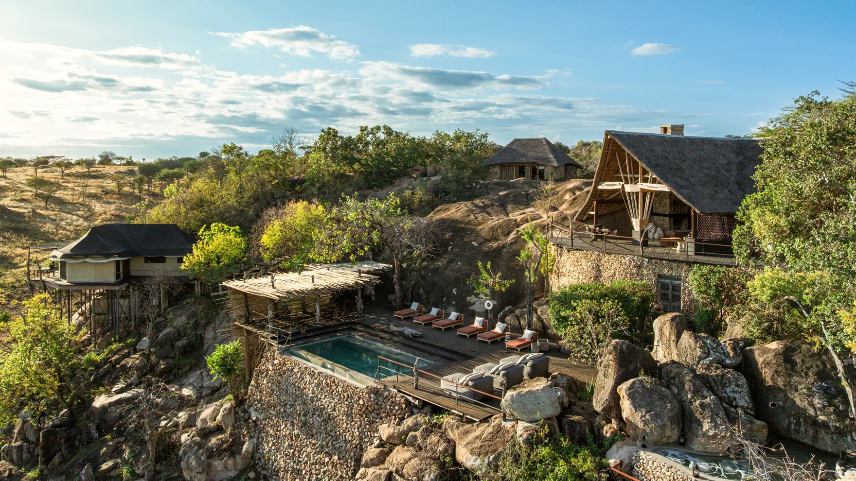 Hillside safari lodge with stone terraces, private pool deck, and elevated tented suites overlooking a rocky landscape.