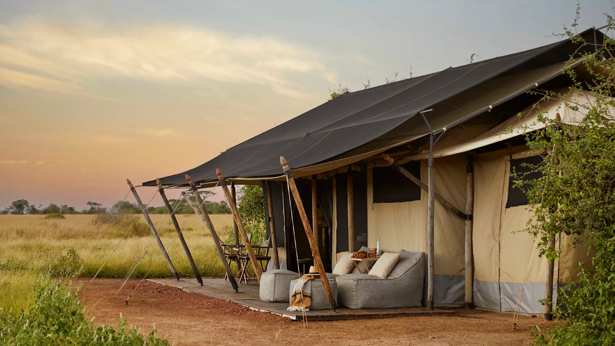 Outdoor seating area with cushioned chairs and a small table under the canopy of a safari-style tent at sunset.