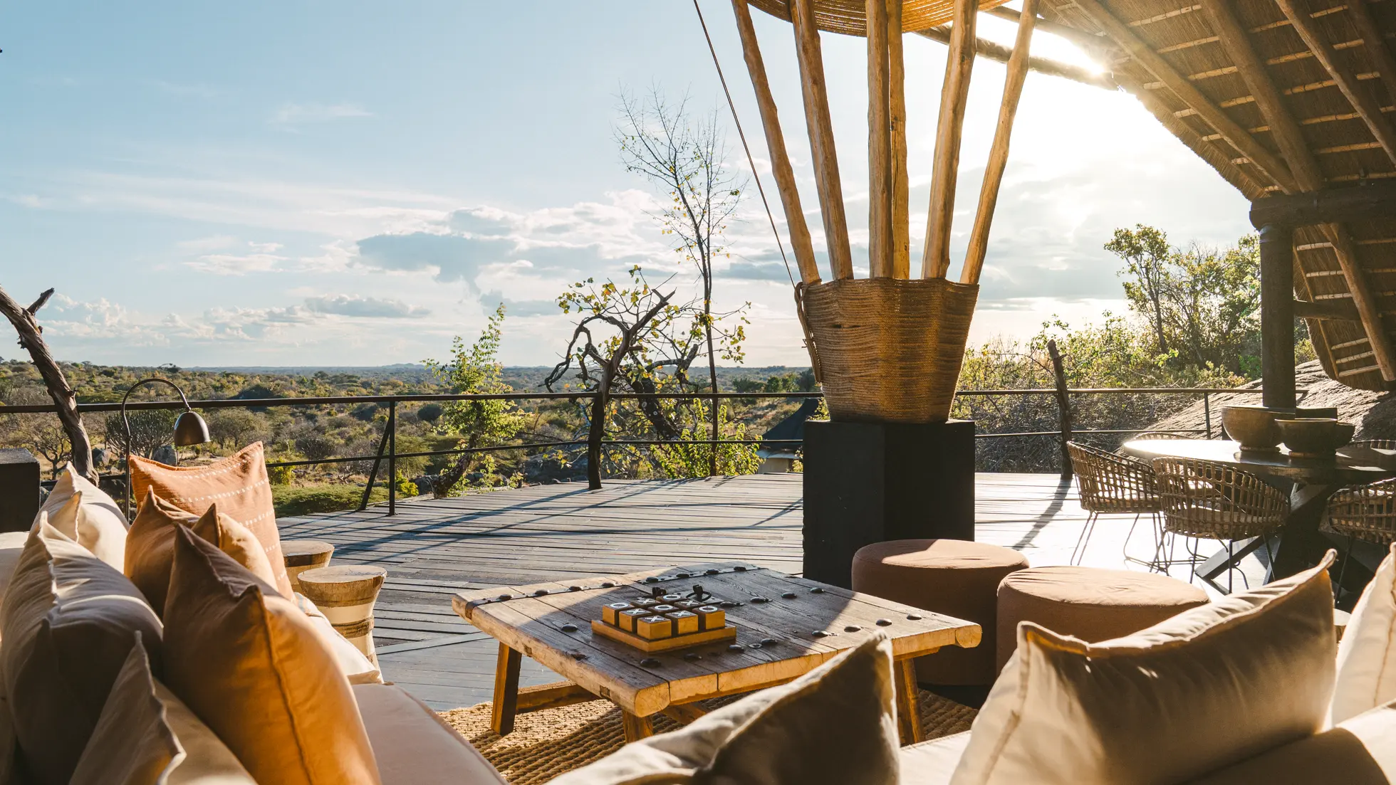 Outdoor wooden deck seating area with cushioned sofas and a scenic view of trees and sky.