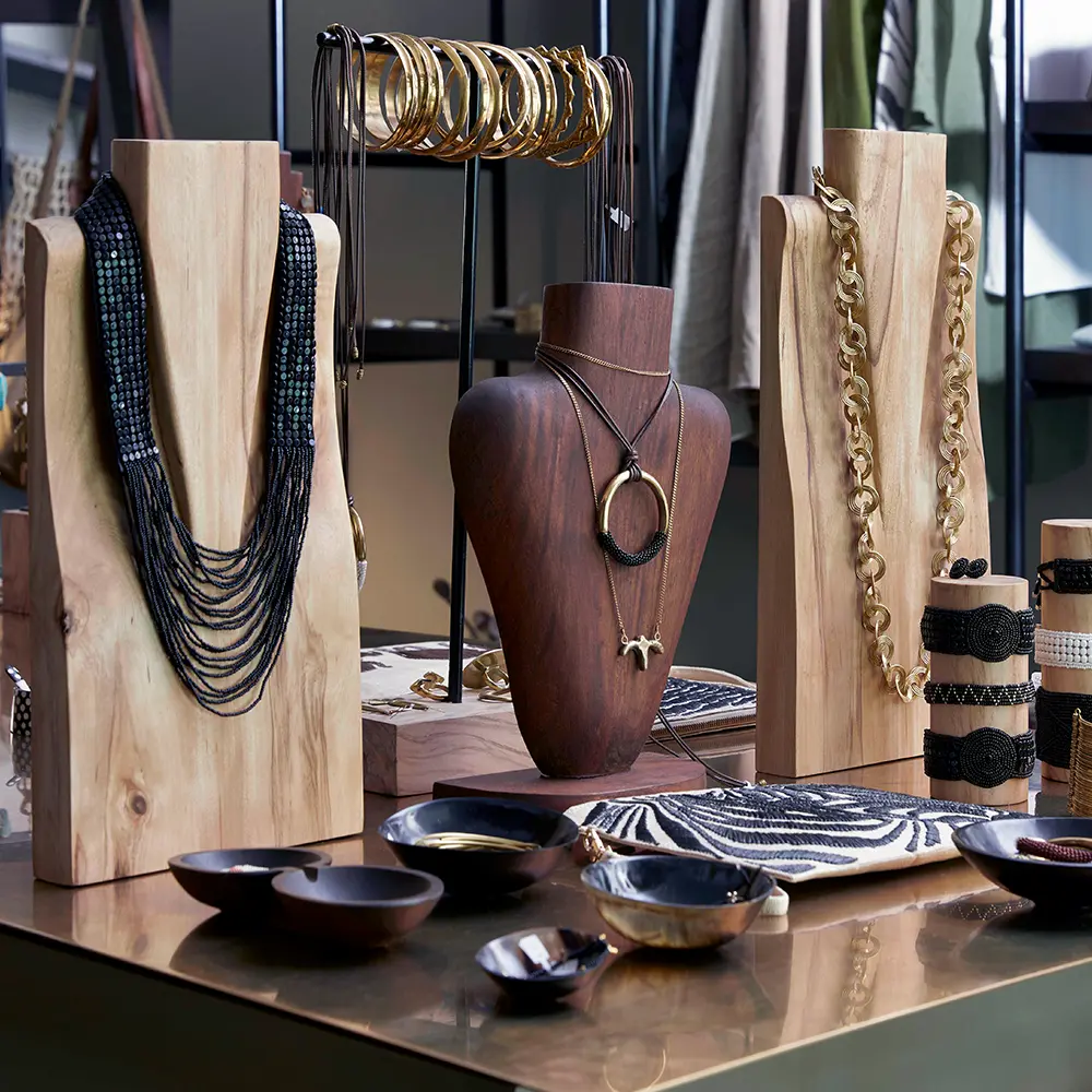 Wooden and dark jewelry displays with black beaded necklaces, gold bracelets, and various black and white accessories on a glass table.
